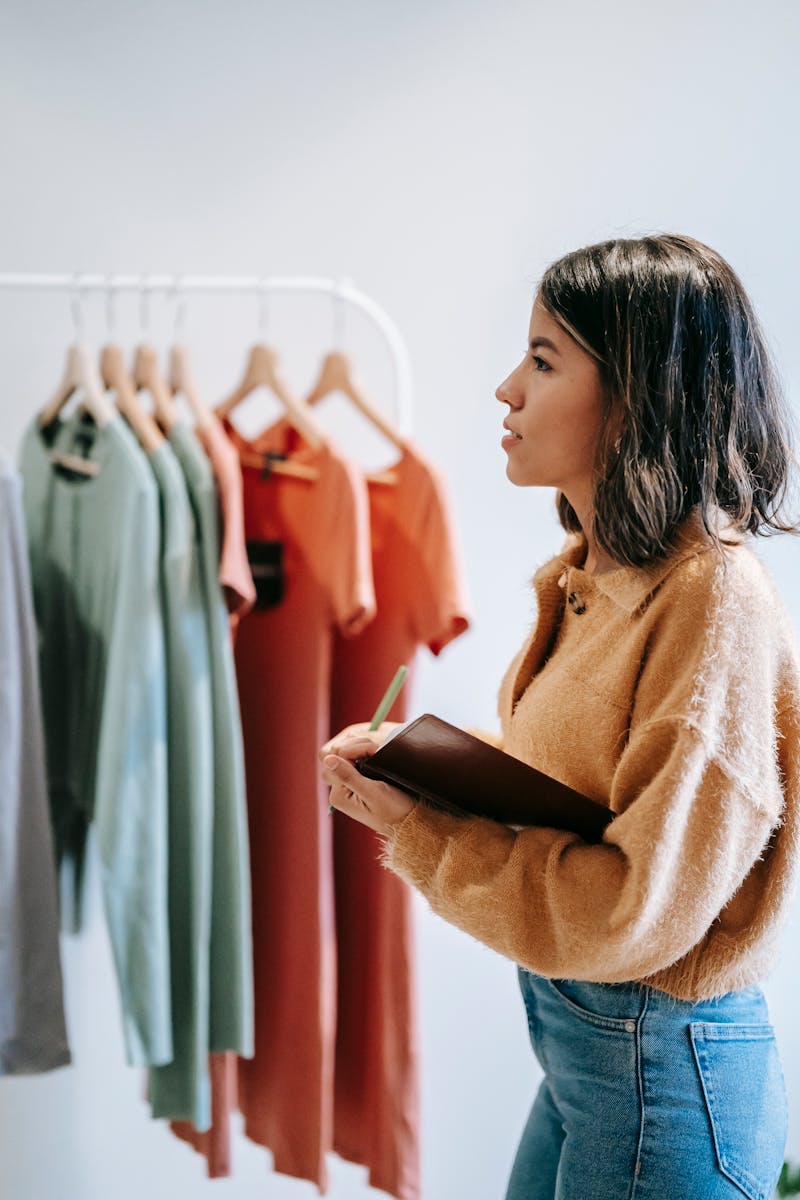 Concentrated lady with notepad near garments on hangers