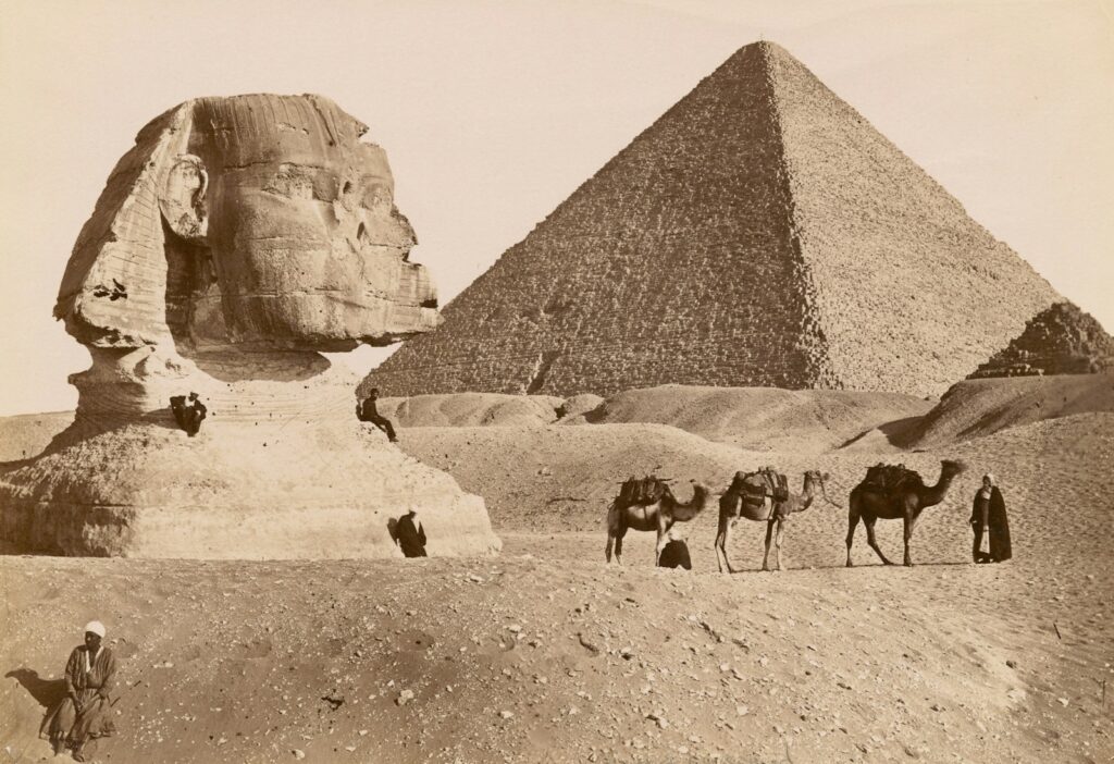 grayscale photo of pyramid and camels in the desert